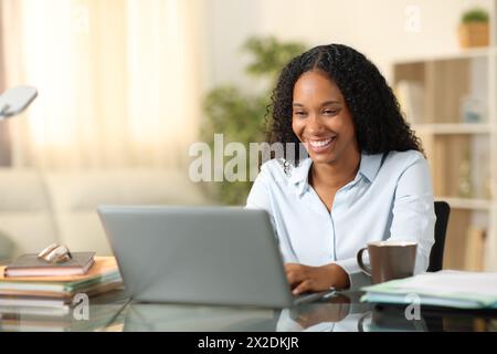 Glücklicher schwarzer freiberuflicher Mitarbeiter, der zu Hause online mit einem Laptop arbeitet Stockfoto