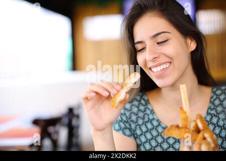 Glückliche Frau isst Hühnerfinger allein in einem Restaurant Stockfoto