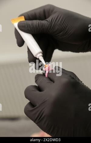 Mikroblading-Künstler in einem schwarzen Handschuh, der Pigment in Tintenringbecher mischt. Nahaufnahme des Pigmentringbehälters und der Tinte für die Augenbrauentätowierung. Schönheitsverfahren Stockfoto