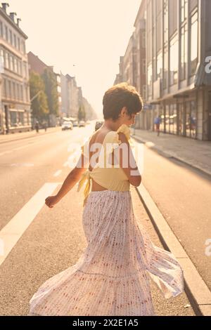 Ein Mädchen mit einem kurzen Haarschnitt in einem gelben Kleid auf den sonnendurchfluteten Straßen Kopenhagens Stockfoto