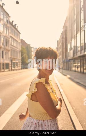 Ein Mädchen mit einem kurzen Haarschnitt in einem gelben Kleid auf den sonnendurchfluteten Straßen Kopenhagens Stockfoto