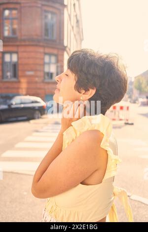 Ein Mädchen mit einem kurzen Haarschnitt in einem gelben Kleid auf den sonnendurchfluteten Straßen Kopenhagens Stockfoto