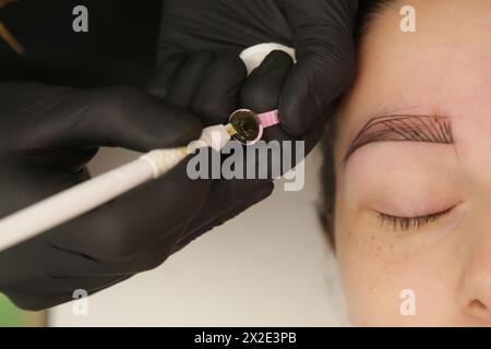 Microblading – halb-permanente Tätowiertechnik für die Augenbrauen, die eine Illusion von einer stärker definierten und volleren Augenbraue erzeugt. Der Künstler macht winziges h Stockfoto