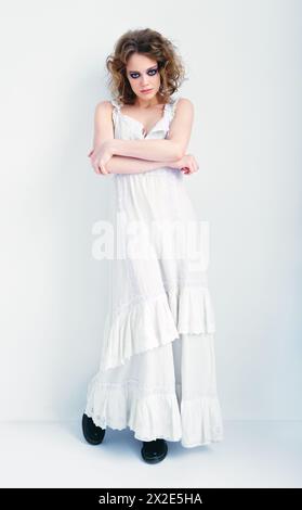 Porträt eines attraktiven seltsamen Mädchens. Schöne, seltsame junge Frau in weißem Kleid, die an der Wand steht Stockfoto
