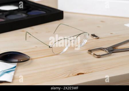 Brillen und Spezialzangen zur Reparatur von Brillengestell, die in der Optikerwerkstatt auf dem Tisch liegen. Augenoptiker und Augenoptiker Augenheilkunde. Sehkonzept Stockfoto