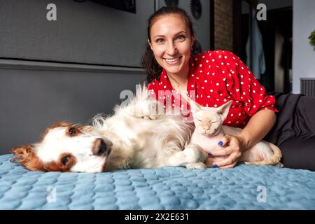 Eine Frau liegt mit einer Katze und einem Hund auf einem Sofa. Liebe für Haustiere Konzept. Stockfoto