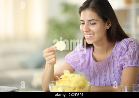 Glückliche Frau isst Kartoffelchips lächelnd zu Hause Stockfoto