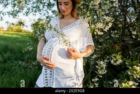 Schöne schwangere Frau in einem weißen Kleid in einem blühenden Garten. Stockfoto