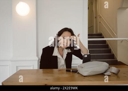 Halb-asiatische Frau rührt Make-up am Telefon vor dem Geschäftstreffen an Stockfoto