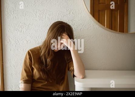 Die überwältigte Frau legt Kopf in die Hand und lehnt sich auf den Tisch Stockfoto