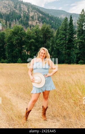 Schöne junge Frau in blauem Sommerkleid mit Cowgirl Hut und Stiefeln Stockfoto