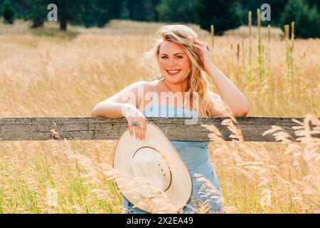 Sonniges Porträt eines Teenager-Mädchens am Holzzaun mit Cowgirl-Hut Stockfoto