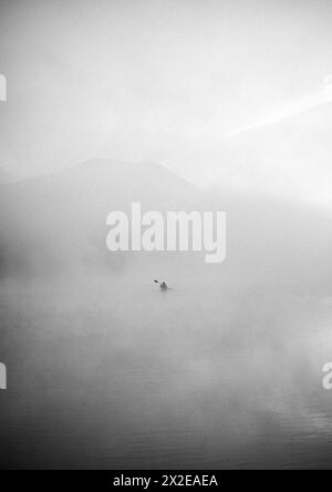 Einsamer Kajakfahrer auf dem See verschwindet in Nebel und Nebel, Maine Stockfoto