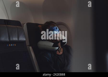 Der Mann schläft während des Fluges in einem Flugzeug und trägt eine Schlafmaske. Stockfoto