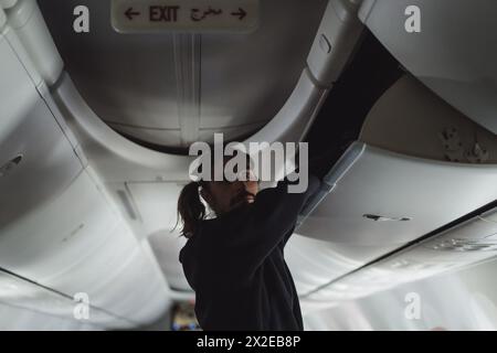 Ein Mann im Flugzeug legt sein Gepäck ins Regal. Stockfoto