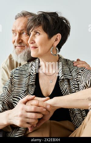 Ein Mann und eine Frau mittleren Alters in stilvoller Kleidung sitzen elegant nebeneinander in einem Studio. Stockfoto