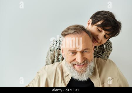 Ein Mann mittleren Alters in stilvoller Kleidung trägt eine Frau auf dem Rücken in einem Studio, das Vertrauen und Teamwork zum Ausdruck bringt. Stockfoto