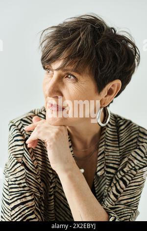 Eine Frau mittleren Alters mit kurzen Haaren, die ein schwarz-weißes Hemd trägt, strahlt Eleganz in einem Studio aus. Stockfoto