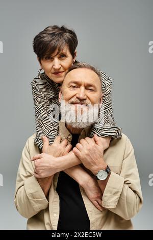 Ein Mann mittleren Alters in stilvoller Kleidung hebt eine Frau in einem Studio auf die Schultern und zeigt Zuneigung und Stärke. Stockfoto