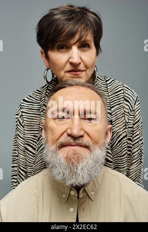 Vorne steht ein bärtiger Mann in stilvoller Kleidung, während eine Frau hinten mit einem geheimnisvollen Ausdruck zublickt. Stockfoto