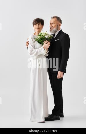 Eine Braut und Bräutigam mittleren Alters in weißer Hochzeitskleidung, die einen Blumenstrauß umschließt und Freude und Liebe ausstrahlt. Stockfoto