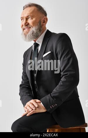 Ein Bräutigam mittleren Alters in einem eleganten Anzug sitzt an seinem Hochzeitstag in einem Studio auf einem Hocker. Stockfoto