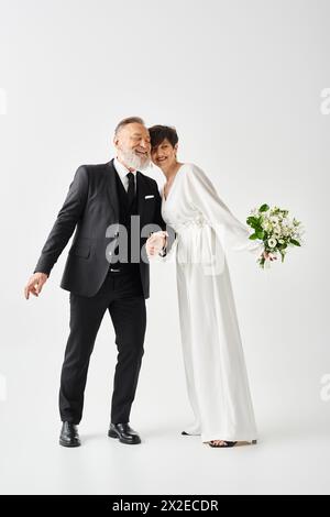 Braut und Bräutigam mittleren Alters, in Hochzeitskleidern gekleidet, posieren in einem Studio, um ihren besonderen Tag festzuhalten. Stockfoto