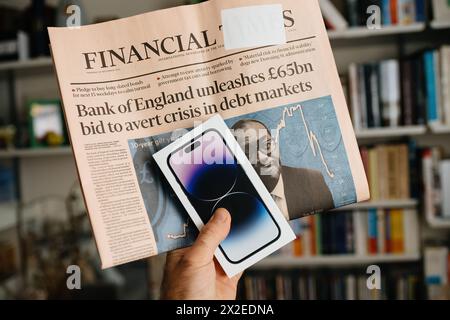 London, Vereinigtes Königreich - 29. September 2022: Ein Mann hält das neueste Apple iPhone 14 Pro und zeigt gleichzeitig die Financial Times mit Schlagzeilen über das 57-Milliarden-Angebot der Bank of Englands, um eine Krise abzuwenden Stockfoto