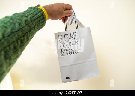 Paris, Frankreich – 7. März 2024: Eine männliche Hand greift eine Papiertüte mit dem Text Little Water, Little Tea, and Magic vor einem scharf weißen Hintergrund Stockfoto