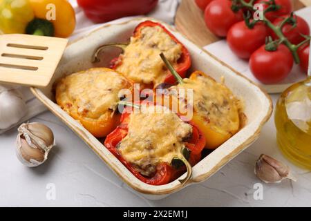 Köstliche gefüllte Paprika in Backform, Spachtel und Zutaten auf weißem, strukturiertem Tisch, Nahaufnahme Stockfoto