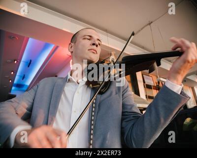 Der Geiger setzt sich mit elektrischer Violine, Leidenschaft in seinem Ausdruck, in lebendiger Beleuchtung ein. Stockfoto