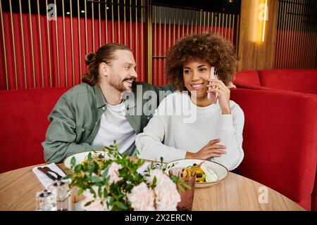 Eine afroamerikanische Frau und ein Mann, der sich tief in Handygesprächen verstrickt hat, während sie an einem Kaffeetisch sitzen. Stockfoto