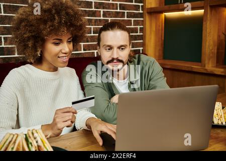 Eine Afroamerikanerin und ein Mann sitzen an einem Tisch, vertieft in ihre Arbeit auf einem Laptop in einem modernen Café. Stockfoto