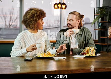 Eine Afroamerikanerin und ein Mann genießen gemeinsam eine Mahlzeit an einem Tisch in einem modernen Café. Stockfoto