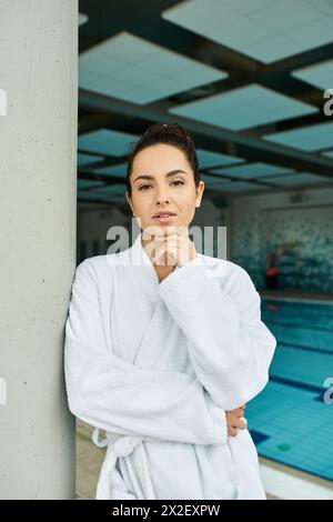 Eine junge Frau in einem Bademantel genießt einen ruhigen Moment am Hallenbad in einem Spa-Ambiente. Stockfoto