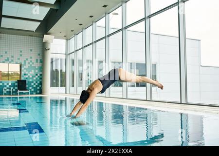 Ein Mann in der Luft, der mit Präzision und Eleganz in einen Swimmingpool taucht und einen Spritzer Wasser erzeugt. Stockfoto