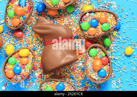 Schokoladenhase und Süßigkeiten, farbige Zuckerstreuseln auf blauem Hintergrund, Draufsicht. Osterkomposition. Osterschokolade-Häschen. Festliche süße Köstlichkeiten. Ch Stockfoto