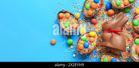 Schokoladenhase und Süßigkeiten, farbige Zuckerstreuseln auf blauem Hintergrund, Draufsicht. Osterkomposition. Osterschokolade-Häschen. Festliche süße Köstlichkeiten. Ch Stockfoto