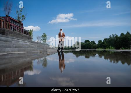 Eine junge Frau, die einen Hijab trägt, steht neben einer großen Pfütze. Stockfoto