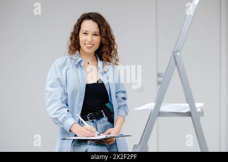 Eine junge, hübsche Designerin bewahrt Dokumente auf, während sie an ihrem Arbeitsplatz steht. Apartment-Renovierung und Designkonzept. Stockfoto