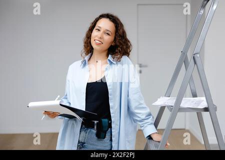 Eine junge, hübsche Designerin bewahrt Dokumente auf, während sie an ihrem Arbeitsplatz steht. Apartment-Renovierung und Designkonzept. Stockfoto