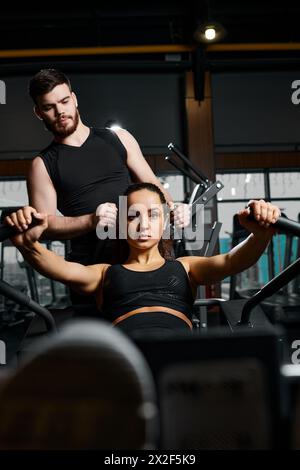 Ein männlicher Trainer hilft einer brünetten Sportlerin bei Übungen in einem Fitnessstudio. Stockfoto