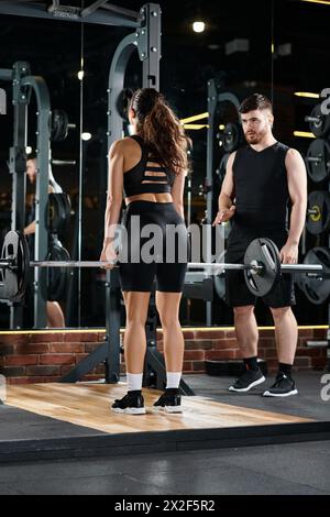 Ein männlicher Personal Trainer unterstützt eine brünette Sportlerin in einem Fitnessstudio mit Trainingsroutinen und Ausrüstung. Stockfoto