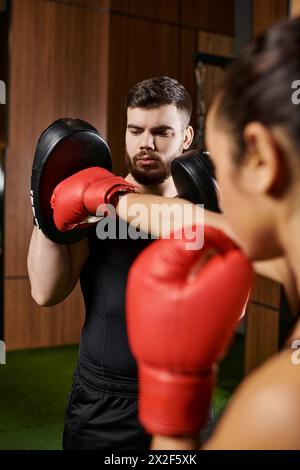 Eine Frau in einem schwarzen Hemd und roten Boxhandschuhen trainiert in einem Fitnessstudio. Stockfoto