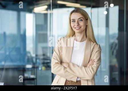 Porträt einer selbstbewussten, professionellen Geschäftsfrau, die lächelt und die Arme in einer hellen, modernen Büroumgebung überkreuzt. Sie strahlt Selbstvertrauen und Professionalität in ihrer stilvollen Kleidung aus. Stockfoto