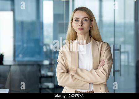 Eine professionelle Geschäftsfrau steht selbstbewusst in einer Unternehmensumgebung, gekleidet in eleganter Freizeitkleidung und mit einem fokussierten Ausdruck. Stockfoto
