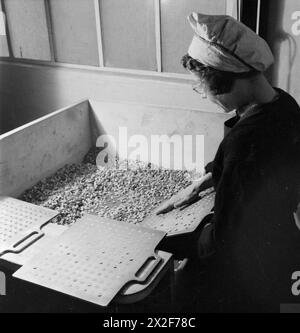 LETTER TO BULLET: BEREINIGTES PAPIER IN GEWEHRPATRONEN VERWANDELN, ENGLAND, 1942 - Eine Kriegsarbeiterin schaufelt kleine Pappscheiben in eine spezielle Metallschale in einer Fabrik irgendwo in Großbritannien. Diese Scheiben bilden den Boden einer Gewehrpatrone Stockfoto