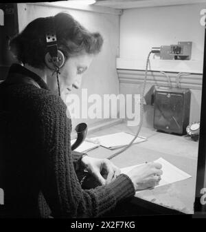 DER WIEDERAUFBAU VON "EINEM VORFALL": ZIVILSCHUTZ-AUSBILDUNG IN FULHAM, LONDON, 1942 - Eine Zivilschutzarbeiterin erhält den Bericht des ARP-Wärters telefonisch im Nachrichtenraum des Kontrollzentrums. Sie trägt ein Headset und eine Lautsprecherröhre, während sie die Nachricht unterdrückt Stockfoto