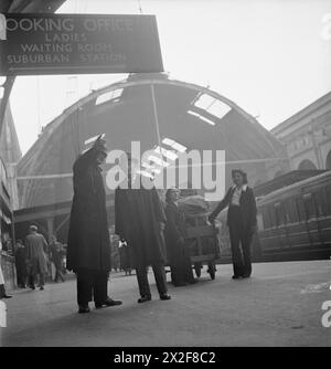 HARRY HARGREAVES GEHT NACH BUCKINGHAM PALACE: VON YORKSHIRE NACH LONDON, UM SEINE BRITISH EMPIRE-MEDAILLE zu HOLEN, 1943 - Harry Hargreaves kommt am Bahnhof King's Cross an und wird von einem Polizisten auf dem Bahnsteig zu seinem Hotel geführt. Hinter ihm entladen zwei weibliche Gepäckträger Stapel Gepäck aus seinem Zug Stockfoto