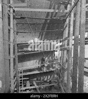 IN Einer BRITISCHEN WERFT: ALLTAG IN DER SCHIFFBAUINDUSTRIE, UK, 1943 - Ein Nieter bei der Arbeit, auf einem Schiff auf den Vorräten einer britischen Werft. Er folgt den Kreidemarkierungen am Rumpf, die anzeigen, wo die Niete angebracht werden sollen. Diese Markierungen werden als „Punktzahl“ des Nieters bezeichnet. Stockfoto